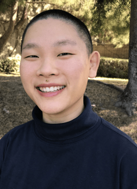 Photo of Graduate Fellow Hanna Jeong smiling outdoors in front of a grassy area with trees. Hanna has close cropped black hair and is wearing a black turtleneck.