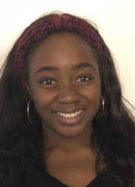 Photo of Program Assistant Khadijah Kareem smiling in front of a white background. Khadijah has long wavy black hair worn loose with a dark red and black headband and wears a black top.